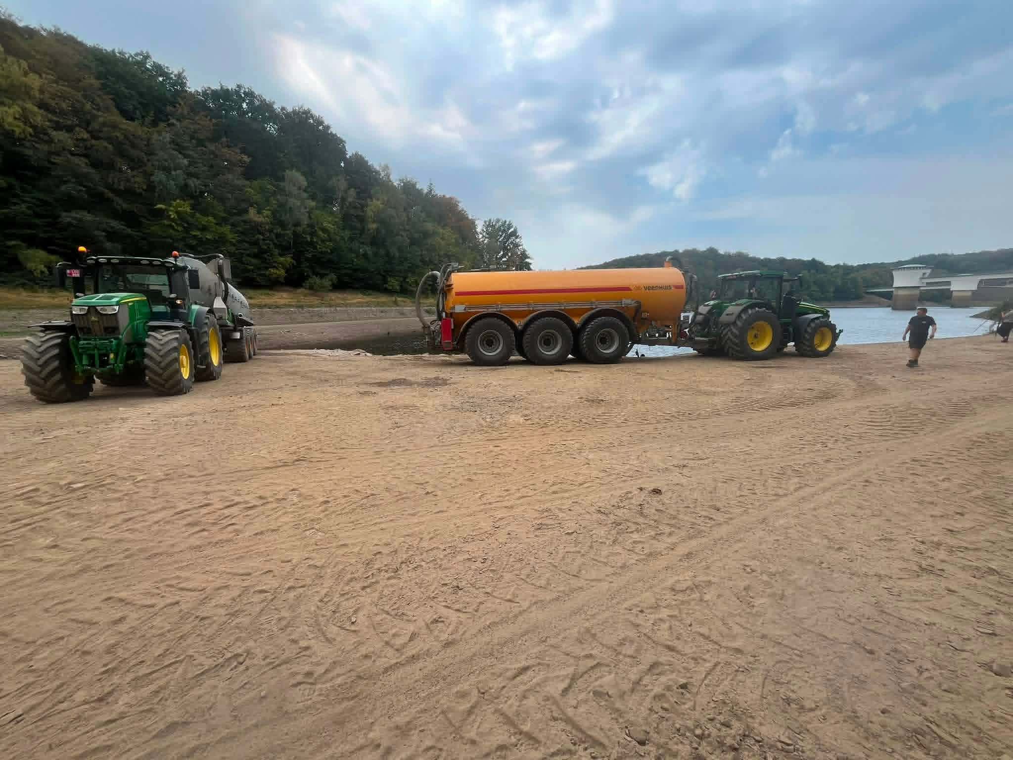 Two farm tractors with tankers on a reservoir shore, loading water for the Hautes Fagnes wildfire